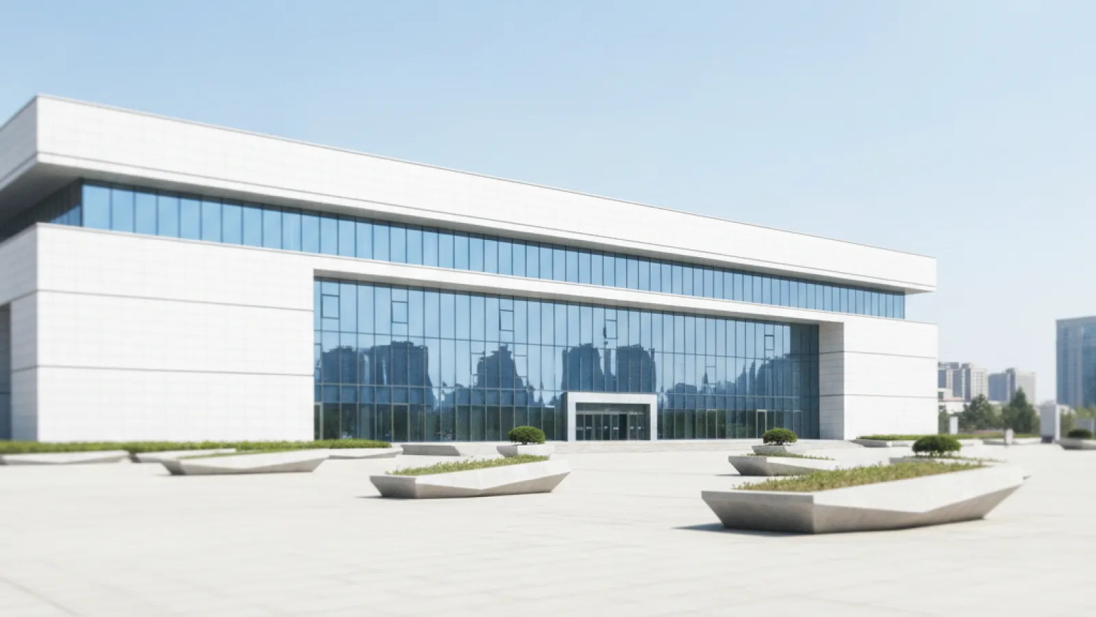 A modern white building with expansive glass windows reflecting city structures stands behind a wide, paved plaza featuring geometric concrete planters with greenery, all under bright daylight.